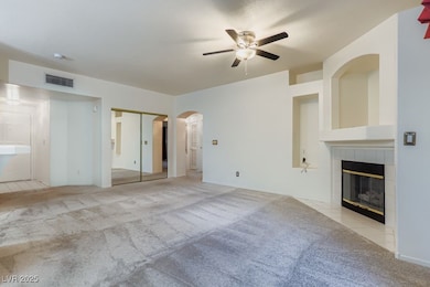 Unfurnished bedroom featuring light carpet, arched walkways, a tile fireplace, ceiling fan, and a closet