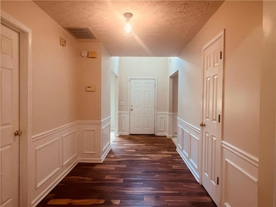 Hallway featuring dark wood finished floors, a textured ceiling, a decorative wall, and a wainscoted wall
