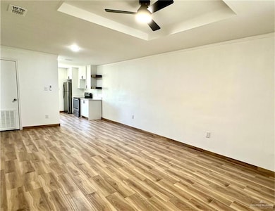 Unfurnished living room featuring a tray ceiling, light wood-style flooring, and a ceiling fan