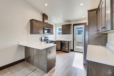 Kitchen featuring a peninsula, dark brown cabinetry, appliances with stainless steel finishes, light wood-type flooring, and vaulted ceiling
