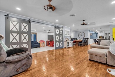 Living area with a barn door, a ceiling fan, light wood-style flooring, recessed lighting, and crown molding