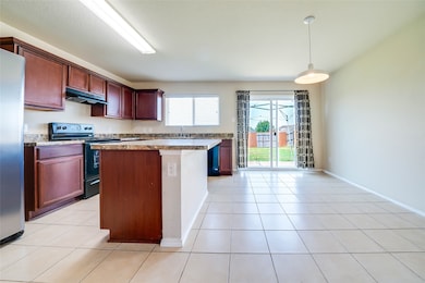 Kitchen featuring black electric range oven, freestanding refrigerator, a kitchen island, pendant lighting, and light tile patterned floors