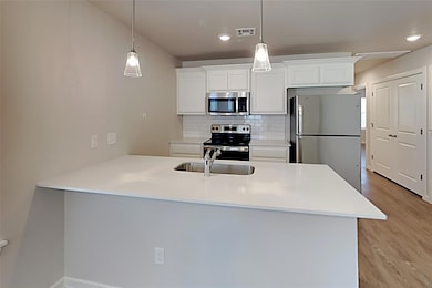 Kitchen featuring stainless steel appliances, a peninsula, backsplash, white cabinetry, and decorative light fixtures