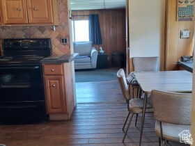 Kitchen featuring electric range, dark wood finished floors, brown cabinets, wooden walls, and tile countertops