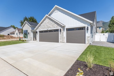 View of front of home featuring a garage, board and batten siding, concrete driveway, stone siding, and a gate