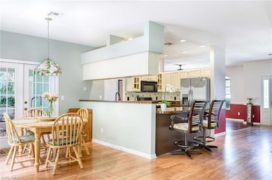 Kitchen with black microwave, stainless steel fridge, cream cabinets, light wood finished floors, and recessed lighting