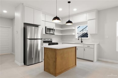 Kitchen with stainless steel appliances, a kitchen island, white cabinets, light countertops, and decorative light fixtures