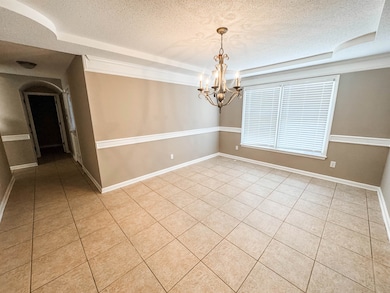 Empty room featuring a textured ceiling, a raised ceiling, light tile patterned floors, a chandelier, and baseboards