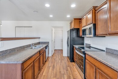 Kitchen with stainless steel appliances, brown cabinetry, dark countertops, light wood-style flooring, and recessed lighting