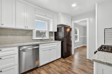 Kitchen featuring white cabinets, black appliances, tasteful backsplash, light stone counters, and dark wood-type flooring