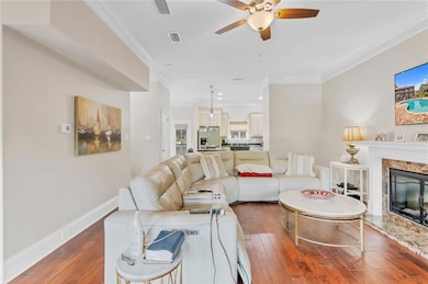 Living area with ceiling fan, hardwood / wood-style flooring, ornamental molding, a high end fireplace, and baseboards