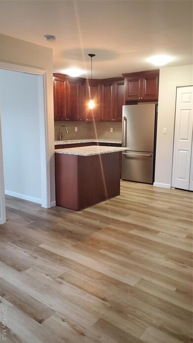 Kitchen featuring fridge, hanging light fixtures, light wood-type flooring, light stone countertops, and tasteful backsplash