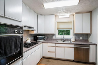 Kitchen with black appliances, under cabinet range hood, a textured ceiling, decorative backsplash, and white cabinetry