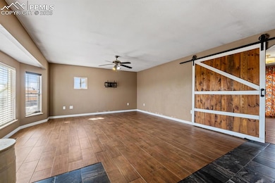 Spare room featuring a barn door, ceiling fan, wood finished floors, and baseboards