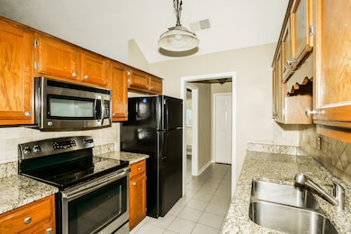 Kitchen with decorative backsplash, appliances with stainless steel finishes, light tile patterned floors, light stone countertops, and brown cabinets