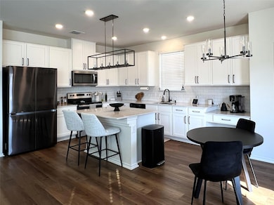 Kitchen with appliances with stainless steel finishes, hanging light fixtures, white cabinets, dark wood finished floors, and decorative backsplash