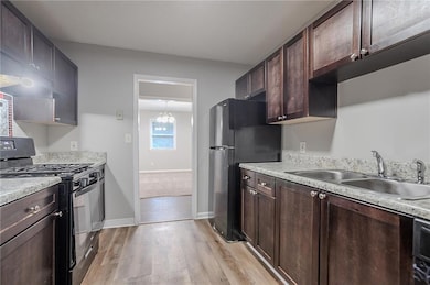 Kitchen with black appliances, a sink, light wood-style flooring, and dark brown cabinetry