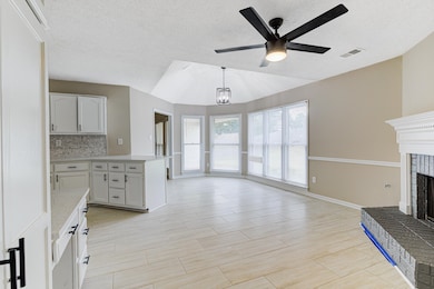 Kitchen with lofted ceiling, ceiling fan, a brick fireplace, light countertops, and open floor plan