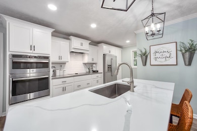 Kitchen featuring appliances with stainless steel finishes, crown molding, decorative backsplash, white cabinetry, and pendant lighting