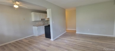Kitchen featuring light wood-style flooring, white cabinets, gas stove, a ceiling fan, and light stone countertops