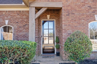 View of exterior entry featuring a shingled roof and brick siding