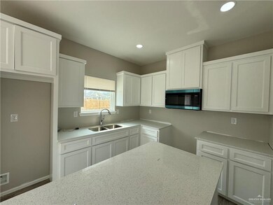 Kitchen with a sink, light stone countertops, white cabinets, and recessed lighting