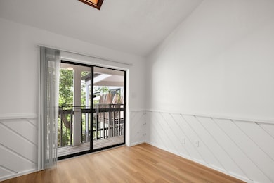 Unfurnished room with light wood-style flooring, wainscoting, and lofted ceiling