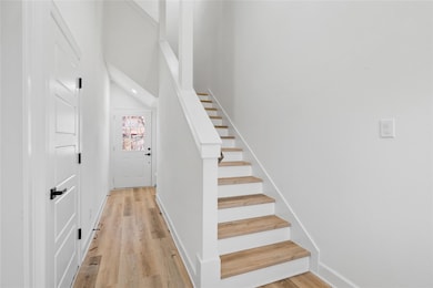 Bright entry with soaring ceilings, wood-look flooring, and a sleek staircase featuring natural wood treads and crisp white risers for a clean, modern look.
