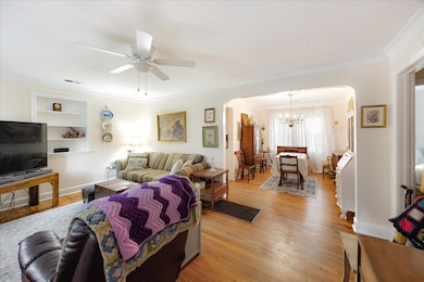 Living room featuring arched walkways, a chandelier, ornamental molding, light wood-type flooring, and ceiling fan