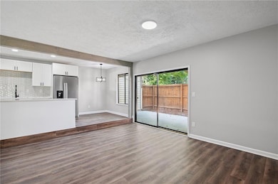 Unfurnished living room with a textured ceiling, dark wood-style flooring, and a chandelier
