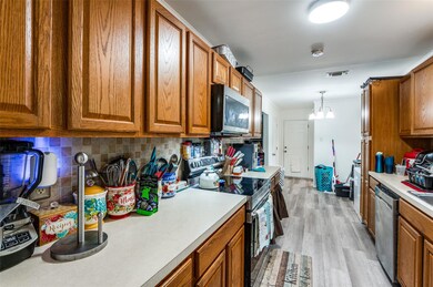 Kitchen featuring light wood-type flooring, a notable chandelier, hanging light fixtures, decorative backsplash, and stainless steel appliances