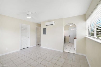 Spare room with an AC wall unit, electric panel, arched walkways, ceiling fan, and light tile patterned floors