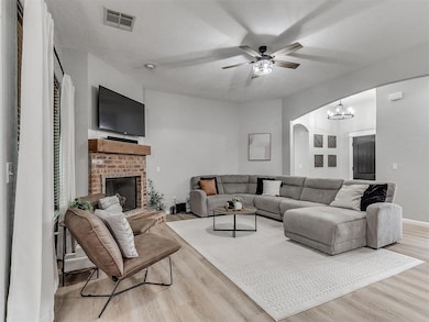 Living room featuring light wood-style flooring, arched walkways, a ceiling fan, a brick fireplace, and a chandelier