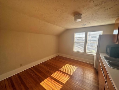 Bonus room with baseboards, wood finished floors, a sink, lofted ceiling, and a textured ceiling