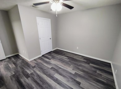 Unfurnished room featuring a ceiling fan, dark woo