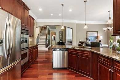 Kitchen featuring stainless steel appliances, crown molding, arched walkways, a sink, and dark wood-style flooring