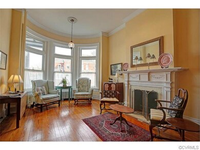 This view of the front parlor/living room shows off the hardwood floors, wonderful bow window, exquisite moulding and gas fireplace