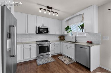 Kitchen featuring appliances with stainless steel finishes, dark wood-type flooring, white cabinets, light stone countertops, and backsplash