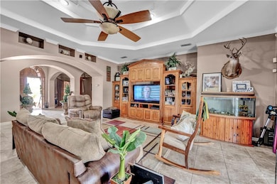 Living room featuring visible vents, ornamental molding, arched walkways, a raised ceiling, and ceiling fan