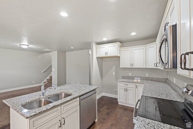 Kitchen featuring stainless steel appliances, light stone countertops, white cabinets, a kitchen island with sink, and a textured ceiling