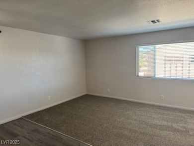 Empty room with dark colored carpet, a textured ceiling, and dark wood finished floors