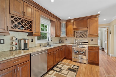 Kitchen with ornamental molding, appliances with stainless steel finishes, light wood-style flooring, light stone counters, and recessed lighting