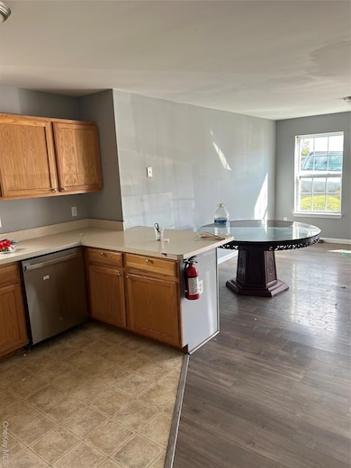 Kitchen featuring light countertops, dishwashing machine, brown cabinetry, a peninsula, and light wood-style floors