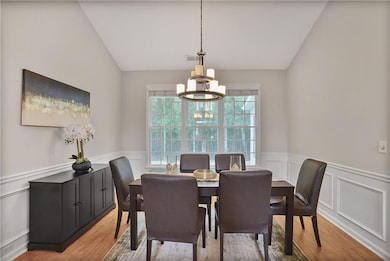 Dining area featuring a chandelier, vaulted ceiling, a wainscoted wall, light wood-type flooring, and a decorative wall