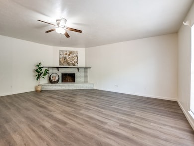 Unfurnished living room with a brick fireplace, light wood-style flooring, and a ceiling fan