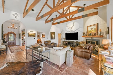 Living area with high vaulted ceiling, a large fireplace, brick floors, a chandelier, and arched walkways
