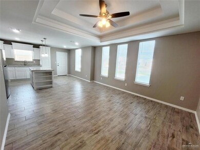 Unfurnished living room featuring a tray ceiling, a ceiling fan, light wood finished floors, and plenty of natural light