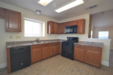 Kitchen with black appliances, light wood-style floors, healthy amount of natural light, and dark countertops