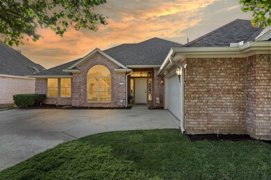 View of front of house with brick siding, a shingled roof, driveway, an attached garage, and a lawn