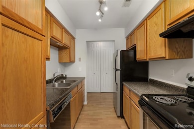 Kitchen with black appliances, light wood-style flooring, dark countertops, and under cabinet range hood